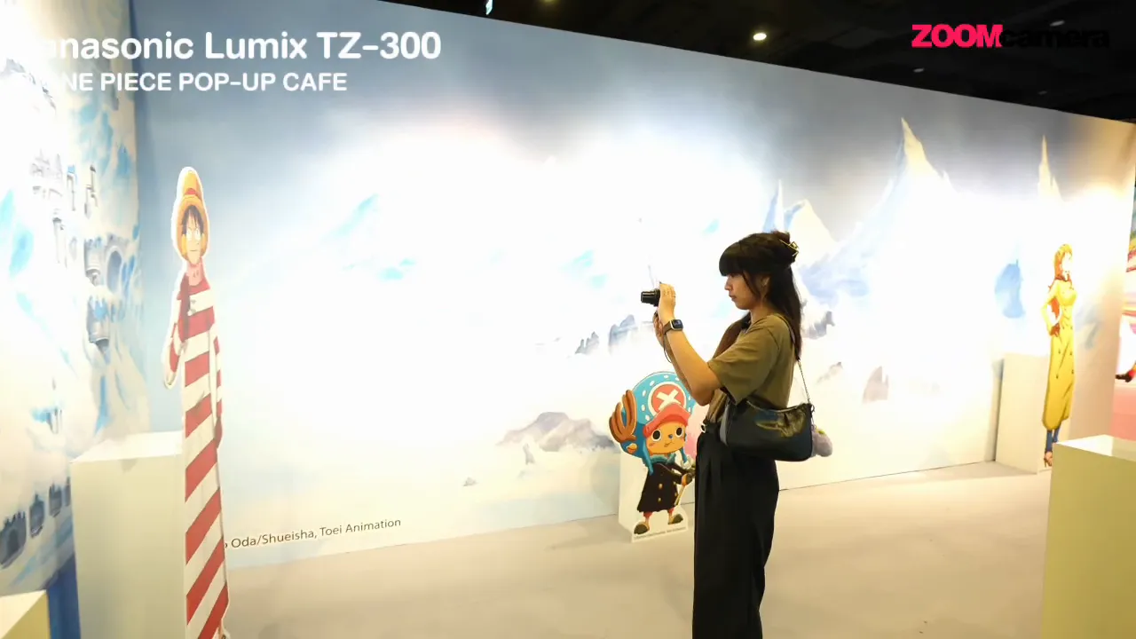 คนยก Panasonic Lumix TZ-300 ถ่ายภาพในบูธ One Piece Pop-Up Cafe เห็นฉากหลังเต็มๆ