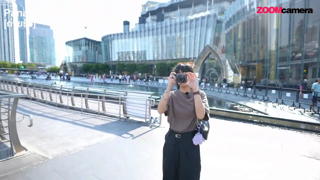 ผู้รีวิวถือ Panasonic Lumix TZ-300 ถ่ายสแน็ปกลางแจ้งพร้อมฉากหลังอาคารและราวกั้น